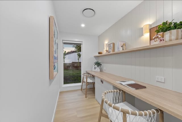 Home office with a long timber desk, built-in storage, matching shelf and garden outlook
